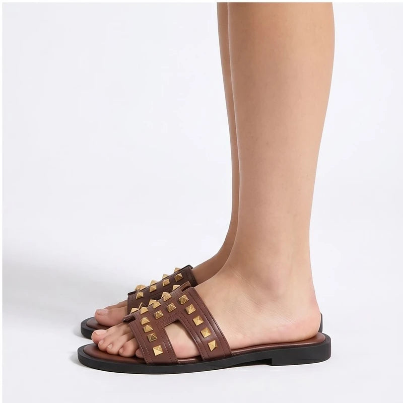 Brown leather slides with gold pyramid studs and a cutout design.