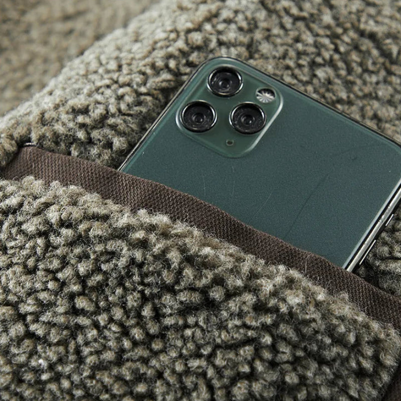 Close-up of a dark green smartphone tucked into a brown woven pocket on a fuzzy gray sherpa jacket.