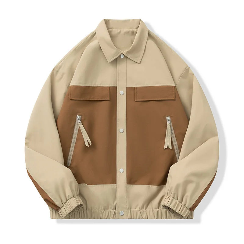 A color-blocked utility jacket in beige and brown, featuring a button-up front, two zippered chest pockets with tassel pulls, and elastic cuffs and hem, shown on a plain white background.
