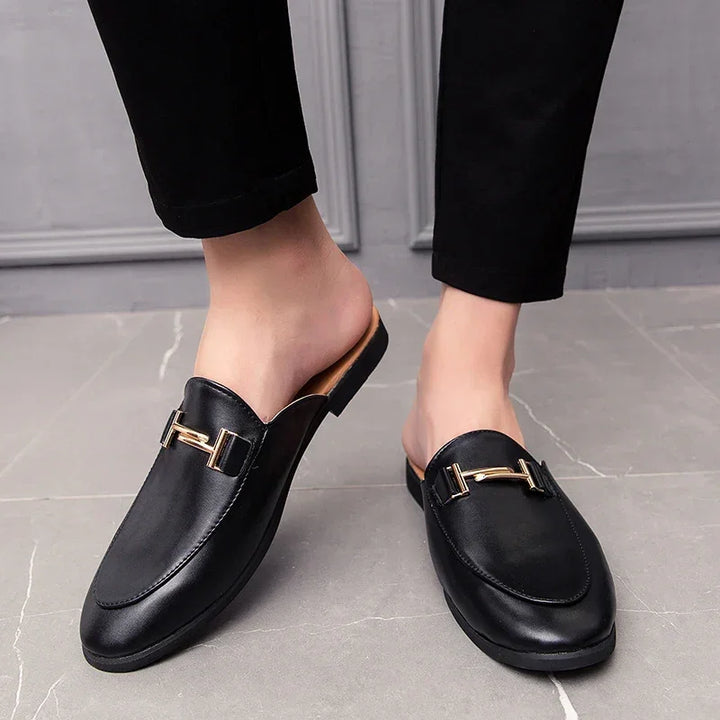 Santino Backless Slide Loafers in black with gold bit hardware, showcasing a sleek slip-on design on a person.