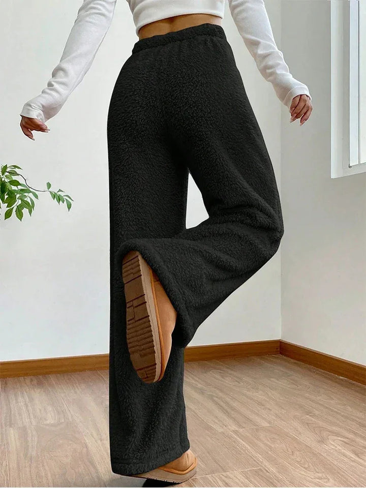 Woman wearing fluffy black sherpa flow sweatpants with wide-leg fit, showing relaxed silhouette and drawstring waist.