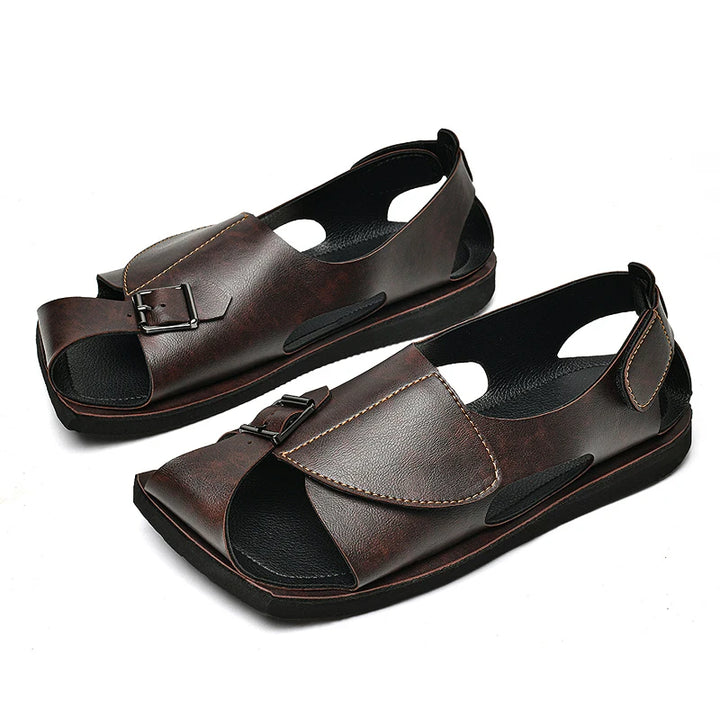 A pair of men's dark brown leather sandals with open toes, double straps with metal buckles, and cutout details, shown on a white background.