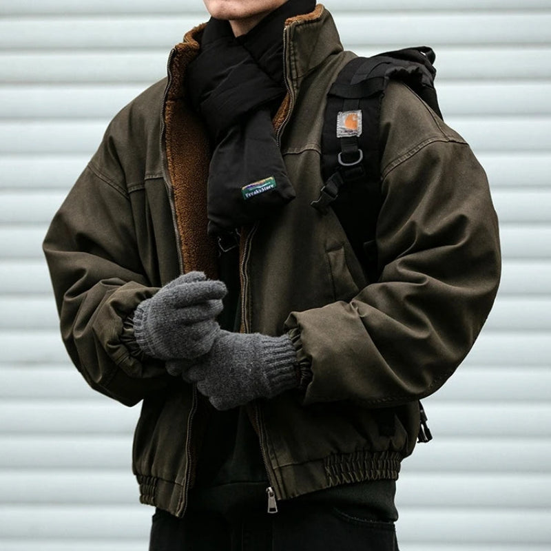 Man wearing an oversized olive green canvas bomber jacket lined with fleece, paired with a black scarf and gray gloves.