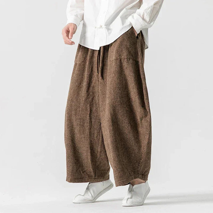 Henderson wide-leg corduroy pants in brown, featuring deep pleats and an elastic waistband for comfort and style.
