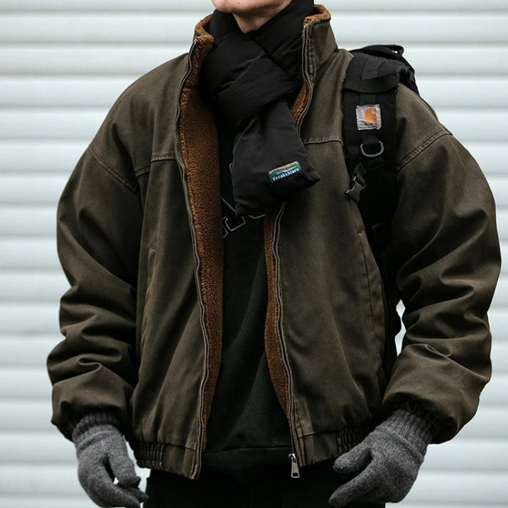 Man wearing an olive brown zip-up canvas jacket with fleece lining, styled with a black scarf and grey knit gloves.