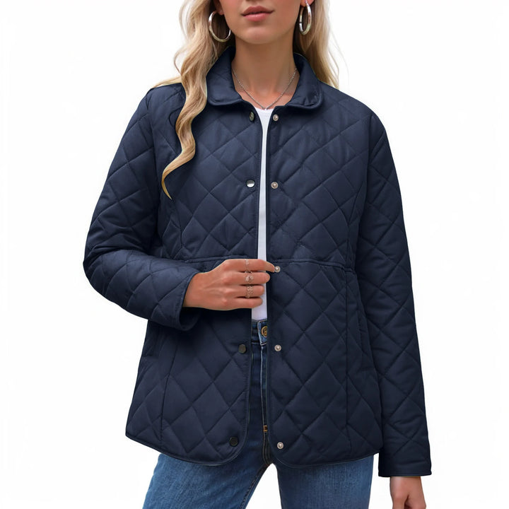 Woman wearing a navy blue quilted jacket with silver snap buttons, a collar, and an elasticated waist over a white shirt.