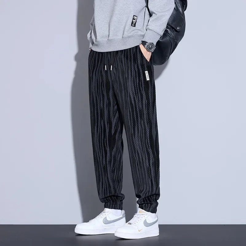 Men's black checkered corduroy pants paired with a gray sweatshirt and white sneakers, showcasing a trendy casual look.