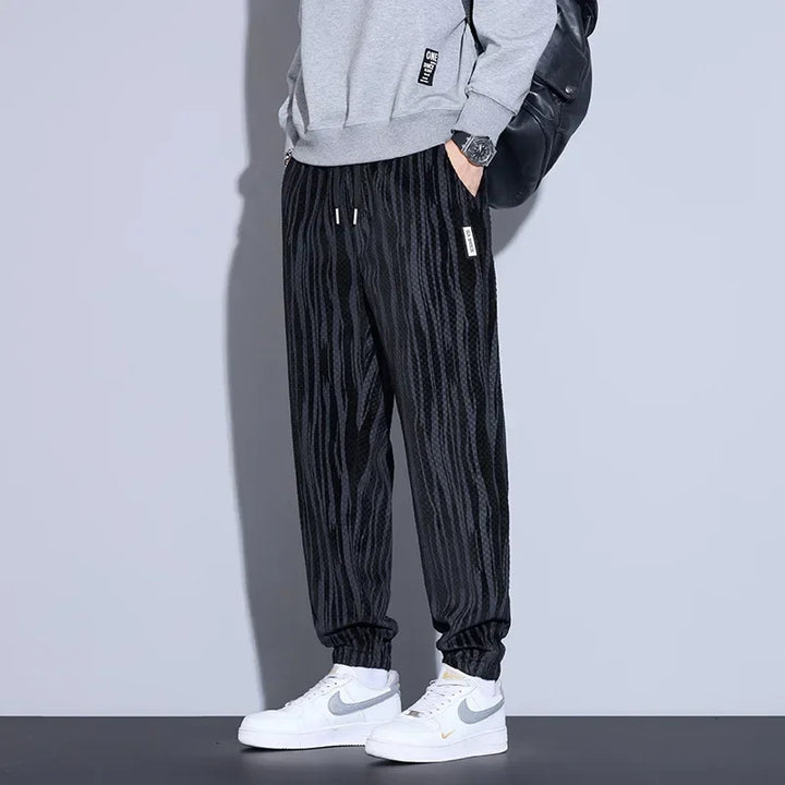 Men's black checkered corduroy pants paired with a gray sweatshirt and white sneakers, showcasing a trendy casual look.