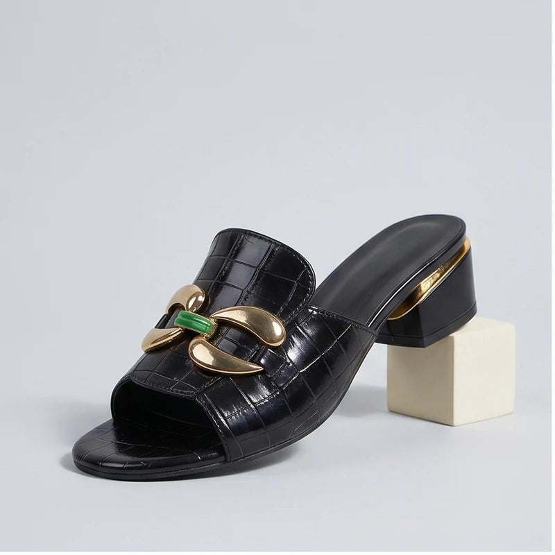 Black embossed leather block heel mules with gold and green embellishments.
