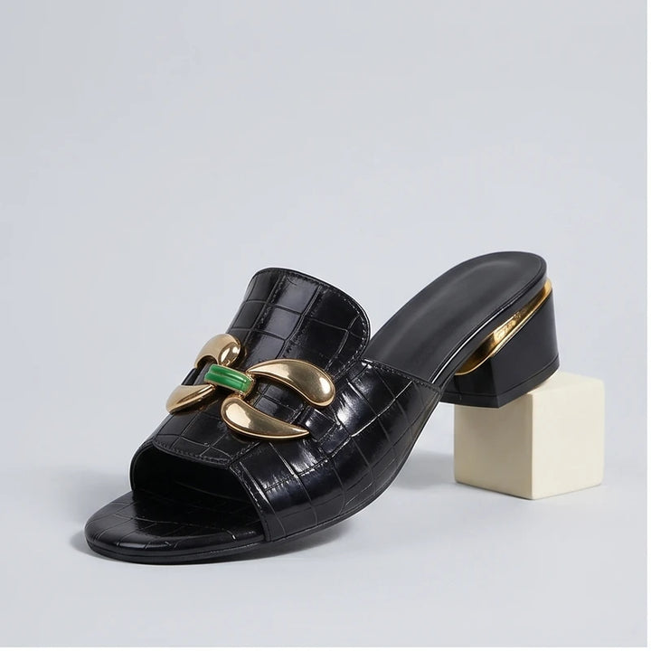 Black embossed leather block heel mules with gold and green embellishments.