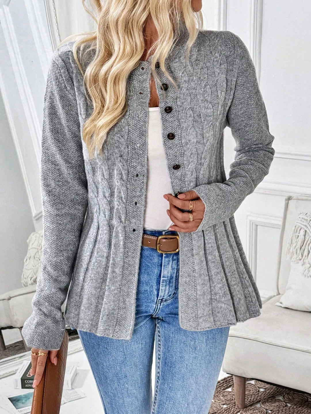 Woman wearing a gray cable knit cardigan with brown buttons, a peplum hem, light blue jeans, and a brown belt.