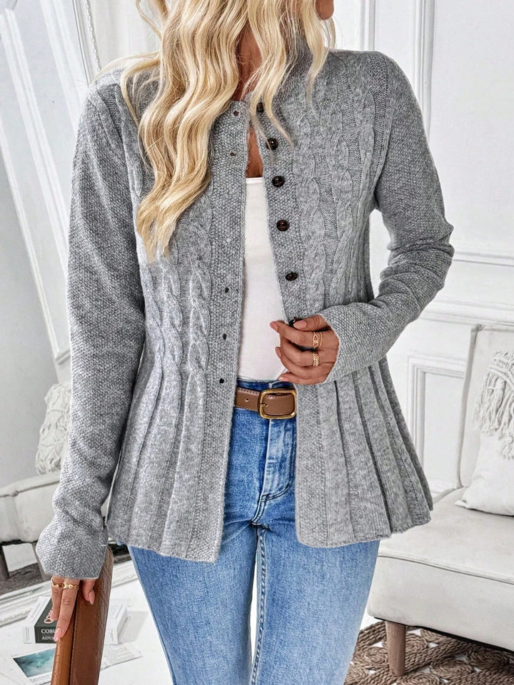 Woman wearing a gray cable knit cardigan with brown buttons, a peplum hem, light blue jeans, and a brown belt.