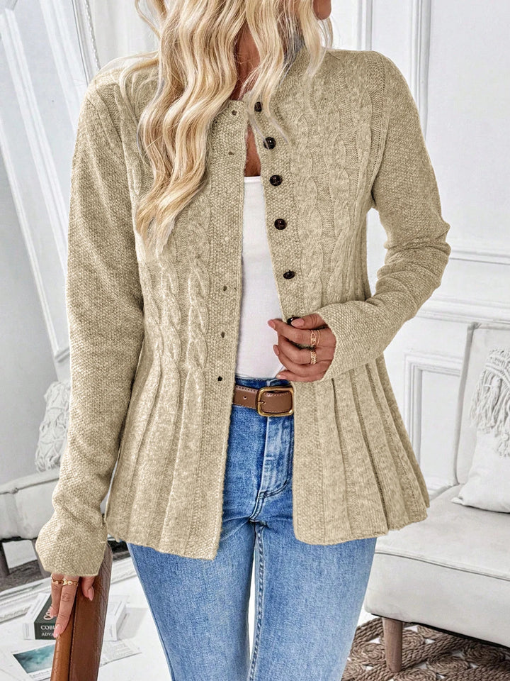 Woman wearing a beige cable knit cardigan with dark brown buttons, a peplum hem, and long sleeves over a white top and blue jeans.