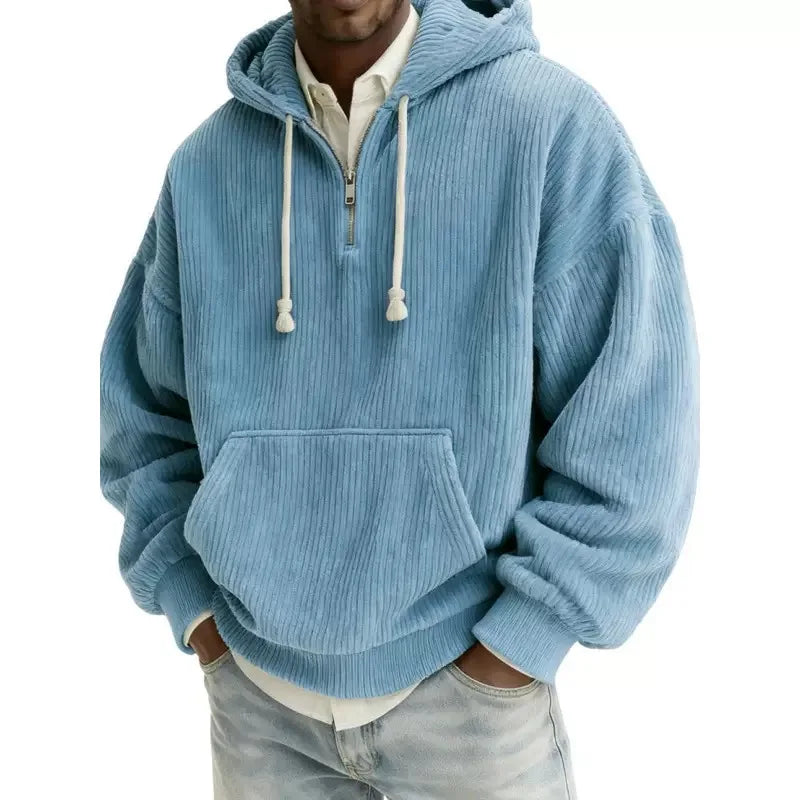 Man wearing an oversized light blue corduroy hoodie with a half-zip neckline, white drawstrings, and front kangaroo pocket.