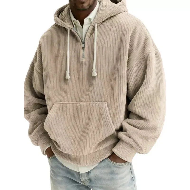 Man wearing a beige corduroy half-zip hoodie with white drawstrings, a front pouch pocket, and light wash jeans.