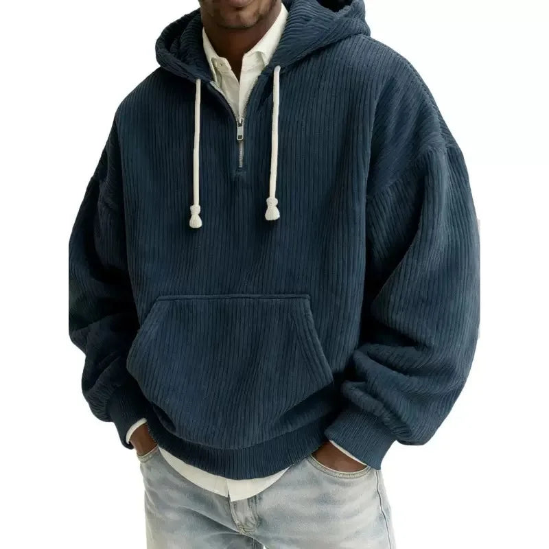 Man wearing an oversized navy blue corduroy hoodie with a half-zip neckline and large front pocket.