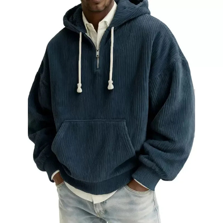 Man wearing an oversized navy blue corduroy hoodie with a half-zip neckline and large front pocket.