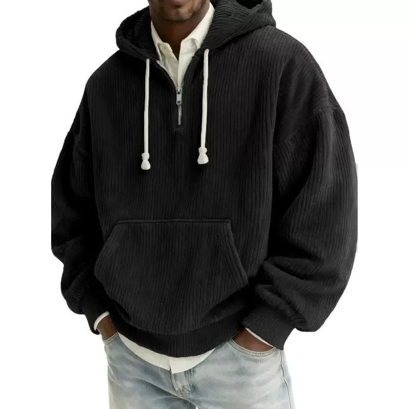 Man wearing a black corduroy half-zip hoodie with white drawstrings, a kangaroo pocket, and light wash jeans.
