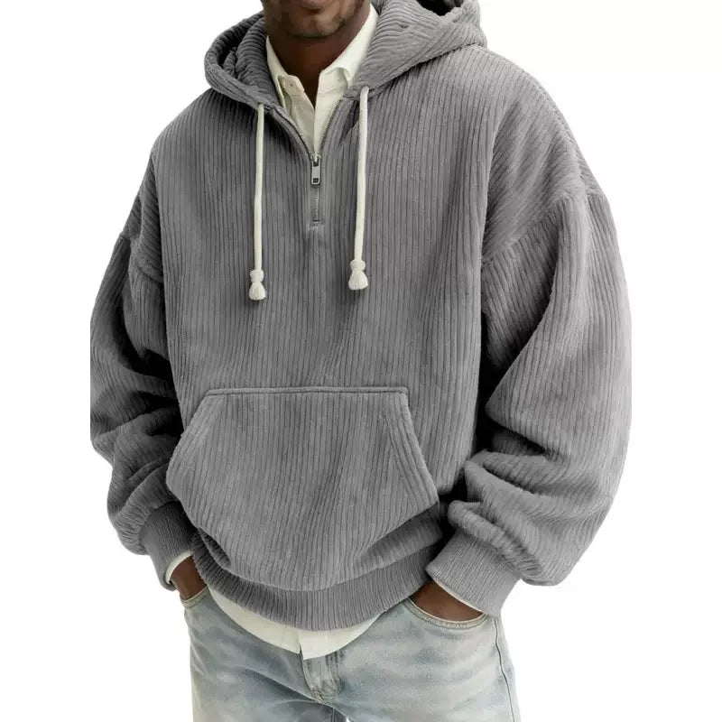 Man wearing an oversized gray corduroy half-zip hoodie with white drawstrings, a kangaroo pocket, and light blue jeans.