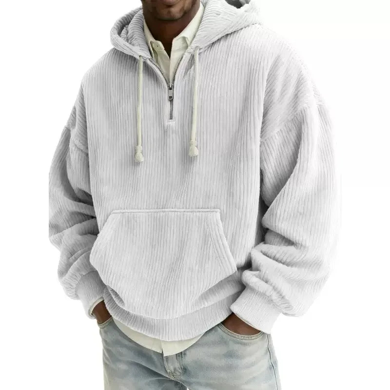 Man wearing a loose-fit light gray corduroy hoodie with a silver half-zip, drawstrings, and a kangaroo pocket.