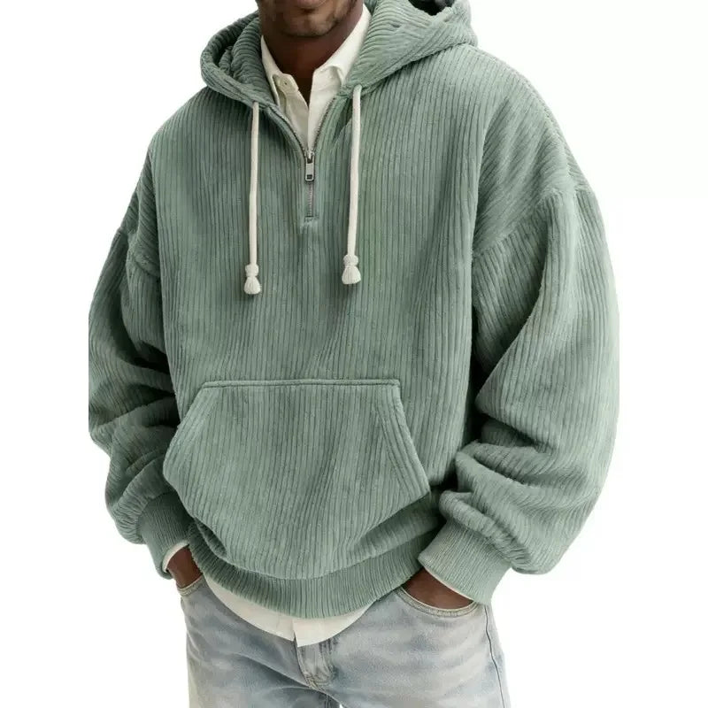 Man wearing an oversized green corduroy half-zip hoodie with white drawstrings and a front kangaroo pocket.