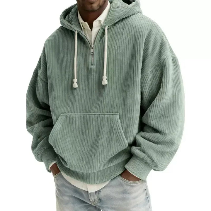 Man wearing an oversized green corduroy half-zip hoodie with white drawstrings and a front kangaroo pocket.