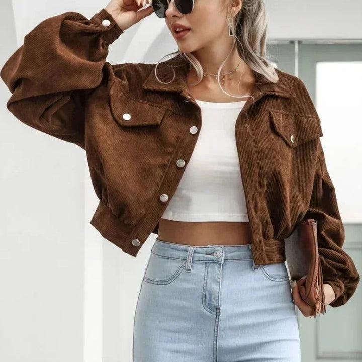 Woman wearing a brown corduroy cropped jacket with voluminous sleeves, silver buttons, and light wash jeans.