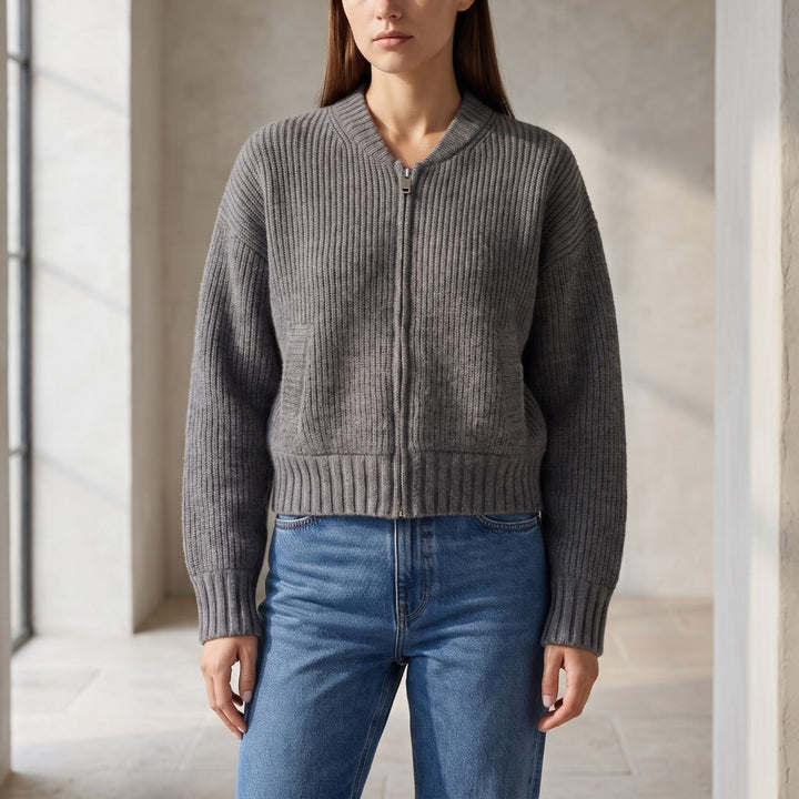 Woman wearing a dark gray ribbed knit cropped cardigan with a silver zipper and light blue jeans.