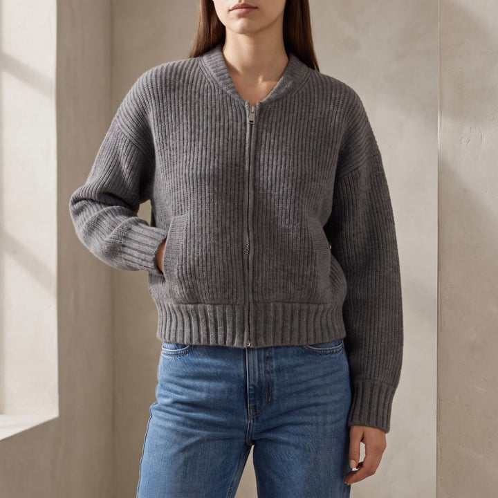 Woman wearing a dark gray ribbed knit cardigan with a silver zipper, standing in jeans with her hand in a pocket.