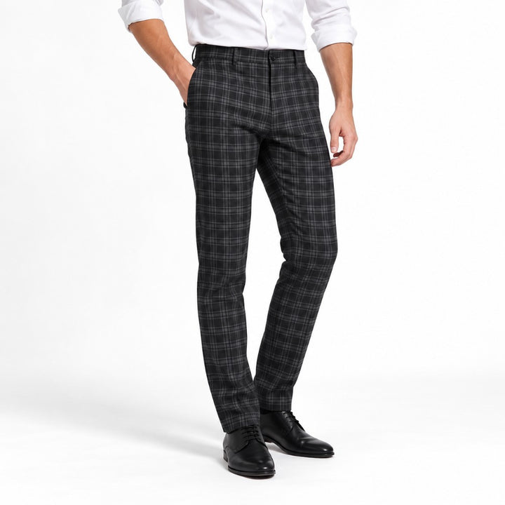 Man wearing a white collared shirt and slim-fit grey and black plaid pants with dress shoes, hand in pocket.