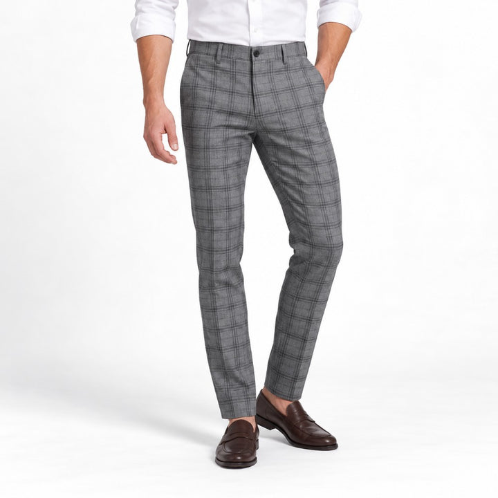 Man wearing slim-fit gray plaid dress slacks with a white shirt and brown leather loafers, against a white background.