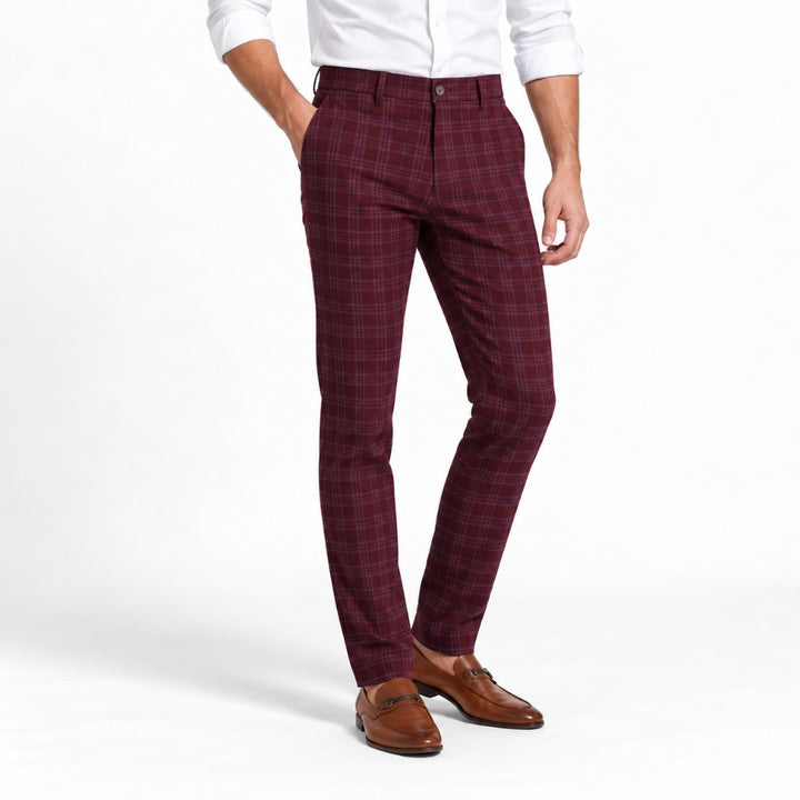 Man wearing slim-fit maroon plaid dress slacks with a white shirt and brown leather loafers, one hand in a pocket.