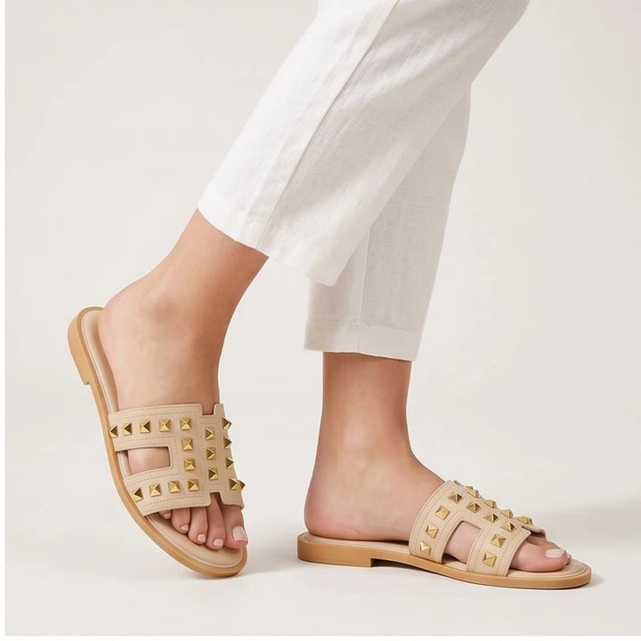 Beige leather slides with gold studs.