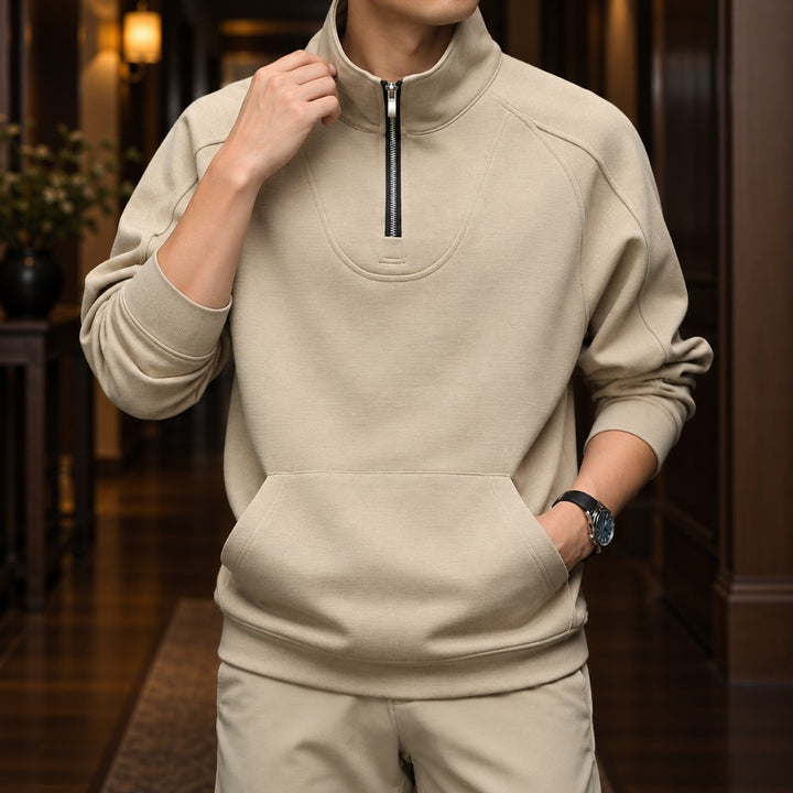 Man wearing a light beige pullover with a half-zipper, stand-up collar, front pocket, and matching pants.