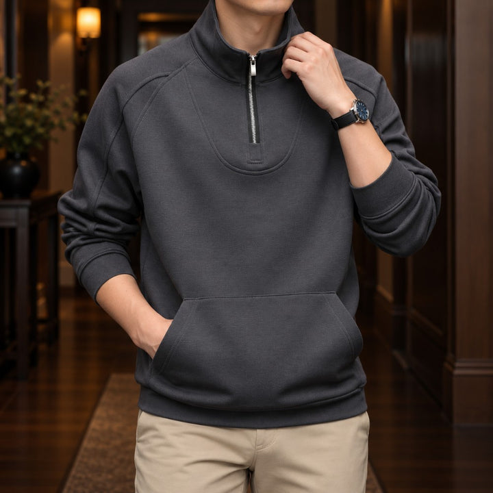 Man wearing a dark gray quarter-zip fleece pullover with a front kangaroo pocket, standing indoors.