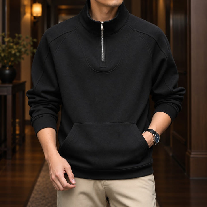 Man wearing a black fleece pullover with a silver quarter-zip, stand-up collar, and front kangaroo pocket.