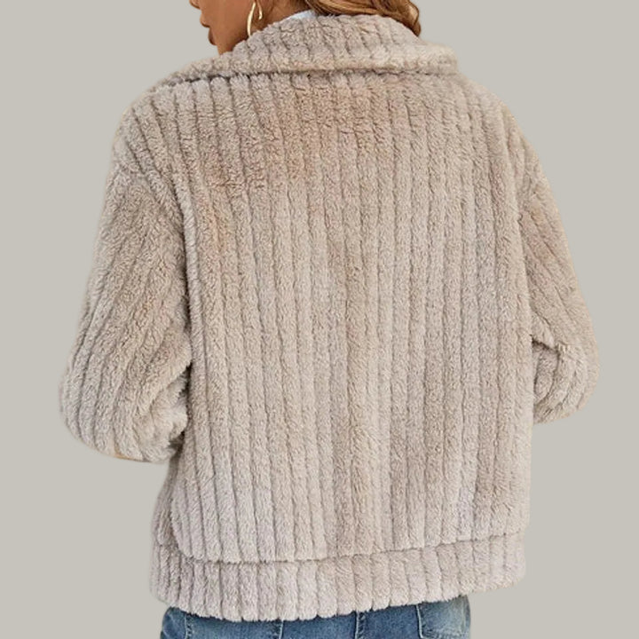 Woman wearing a beige faux fur ribbed jacket with a wide collar and elastic hem, seen from the back.
