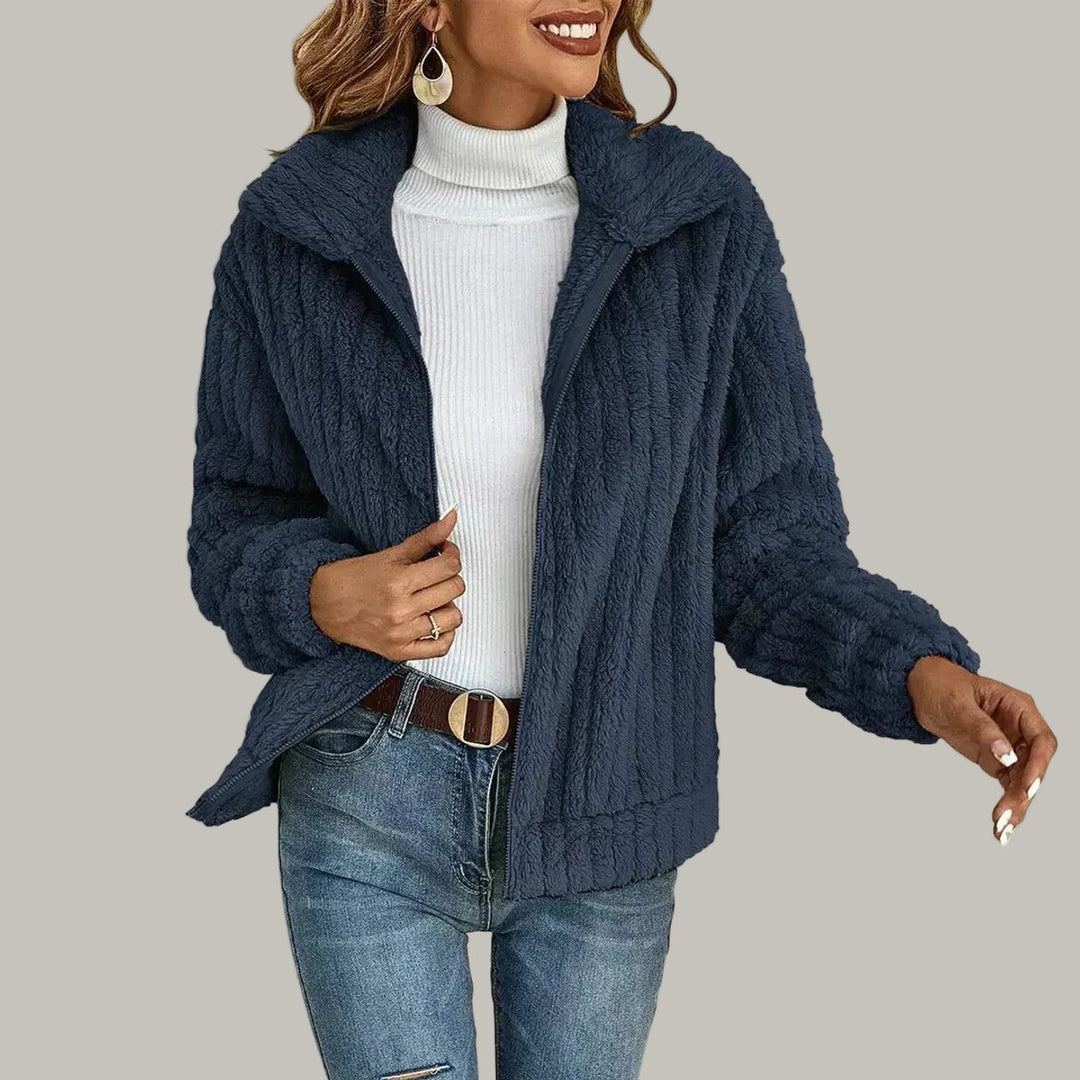 Woman wearing an open navy blue textured fleece zip-up jacket over a white turtleneck and blue ripped jeans.