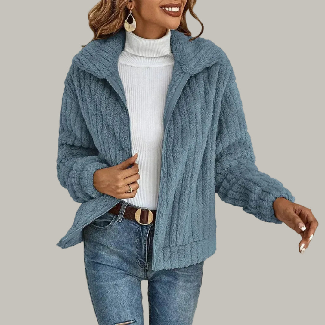 Woman wearing a light blue textured fleece jacket over a white turtleneck and blue jeans with a brown belt.