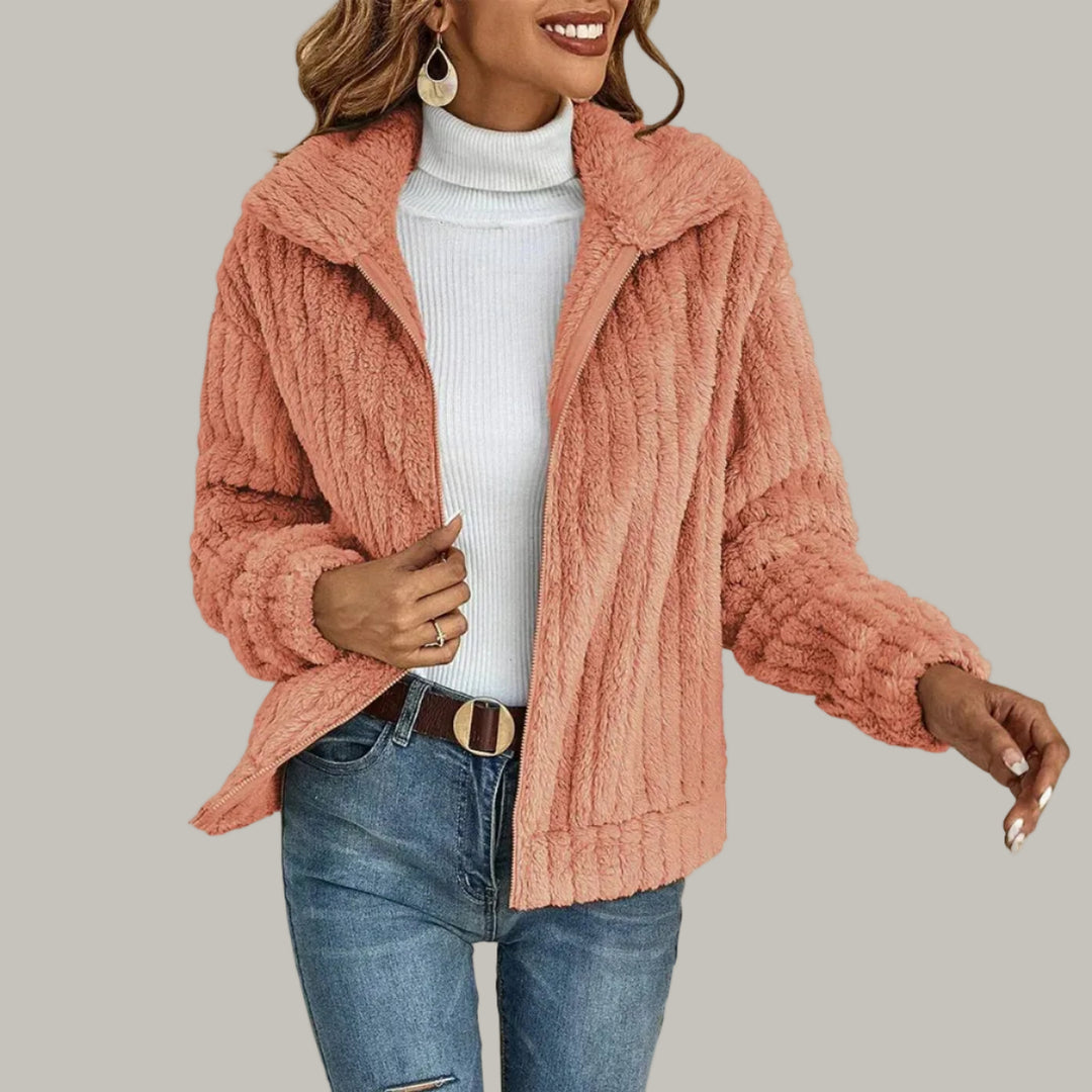 Woman wearing a peach-pink textured fleece zip-up jacket with an open collar over a white turtleneck and blue jeans.