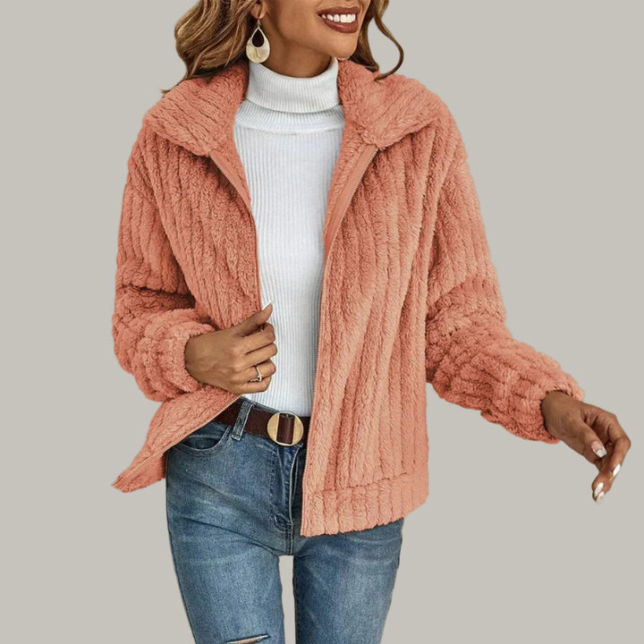 Woman wearing a peach-pink textured fleece zip-up jacket with an open collar over a white turtleneck and blue jeans.