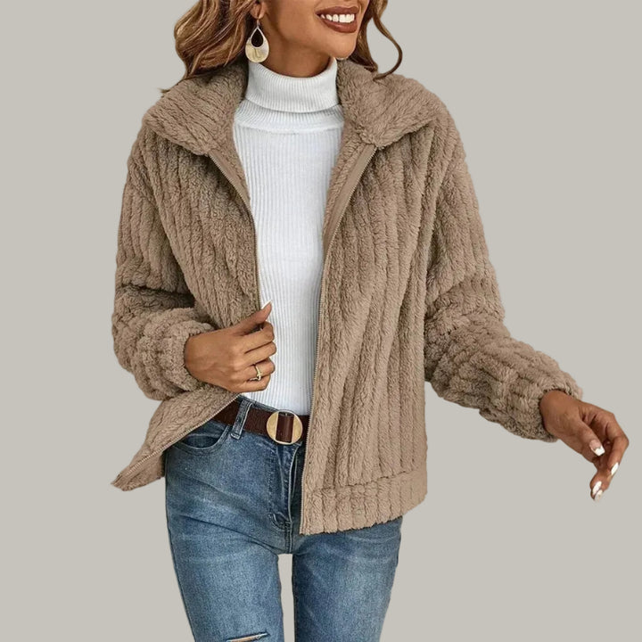 Woman wearing a light brown shaggy fleece zip-up jacket with a wide collar over a white turtleneck and blue jeans.