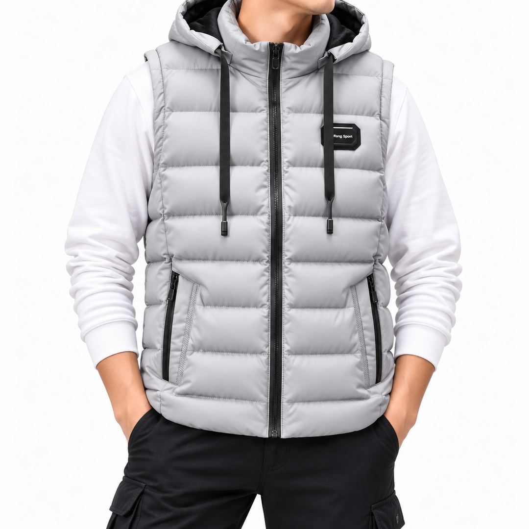 Man wearing a light gray hooded puffer vest with black zippers and drawstrings over a white sweatshirt and black pants.