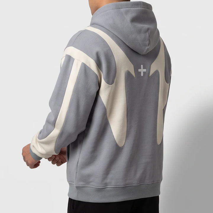 Man wearing an oversized grey hoodie featuring cream curved back paneling and a small white cross against a white backdrop.