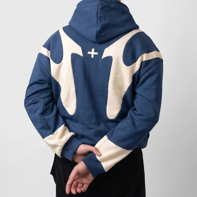 Man wearing a blue hoodie with cream curved contrast panels and a small cross on the back.
