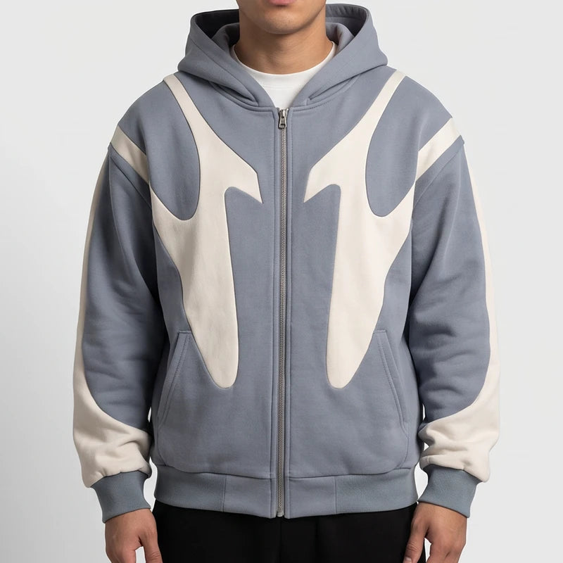 Man wearing a slate blue zip-up hoodie featuring cream abstract panels and side pockets against a white studio background.
