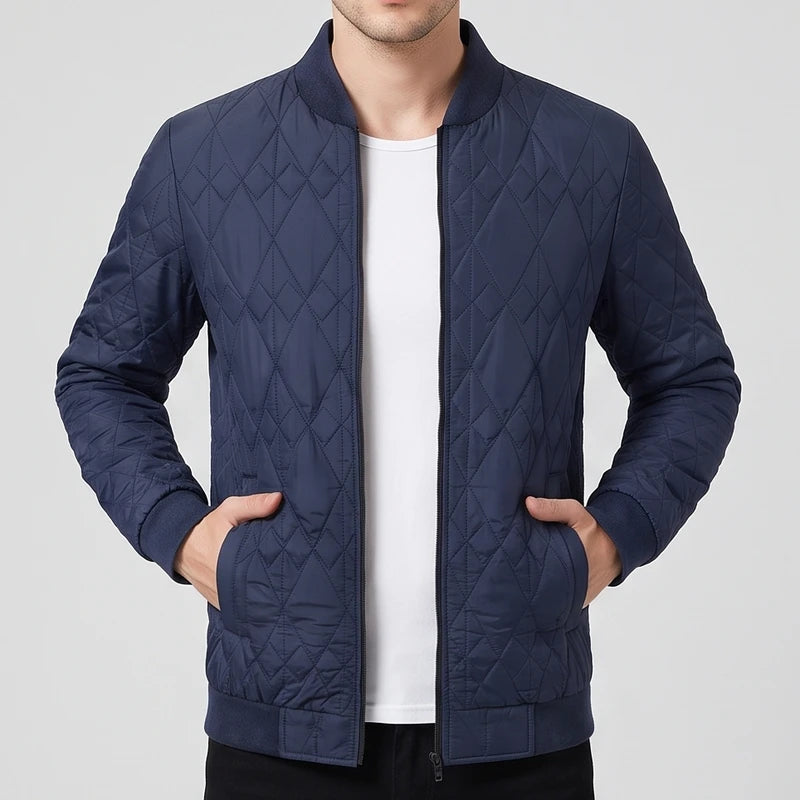 Man wearing a dark navy quilted bomber jacket with diamond pattern, ribbed trim, and a black zipper, hands in pockets.