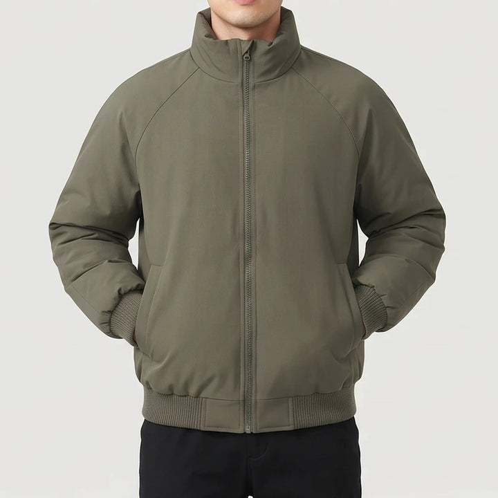 Man wearing a dark olive green bomber jacket with raglan sleeves, ribbed cuffs and hem, and a fully zipped stand collar.