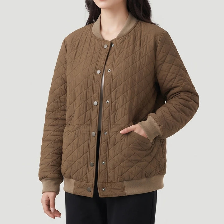 Woman wearing a quilted brown bomber jacket with ribbed tan trim, snap buttons, and her hand in a front pocket.