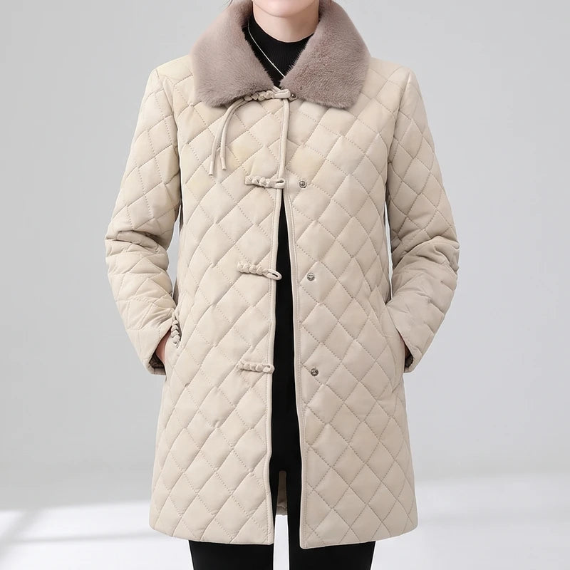 Woman wearing a long, quilted cream jacket with a faux fur collar and traditional frog closure buttons over a black top.